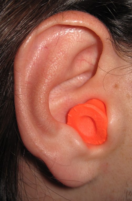 Foam earplugs resting on a nightstand beside a bed